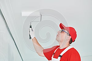 Painter worker with roller painting ceiling surface into white