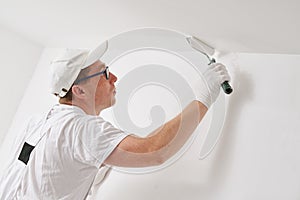 Painter worker with roller painting ceiling surface into white