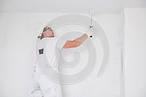 Painter worker with roller painting ceiling surface into white