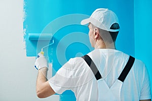 Painter worker with roller painting wall surface into color photo