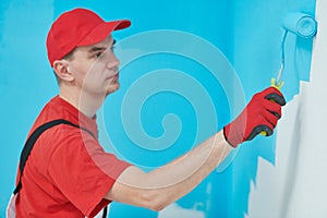Painter worker with roller painting wall surface into color