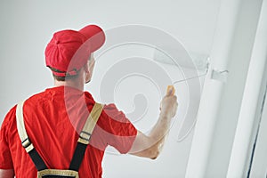 Painter worker with roller painting wall surface into white