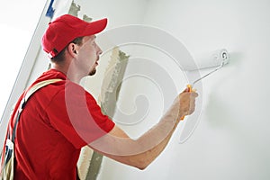 Painter worker with roller painting wall surface into white