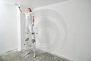 Painter worker on stilts with roller painting ceiling into white