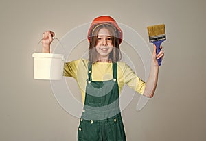 painter in workshop. renovation and repair. teen girl in helmet and boilersuit with painting brush and bucket. child