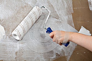 Painters hand holds paint roller, painting wall with white color