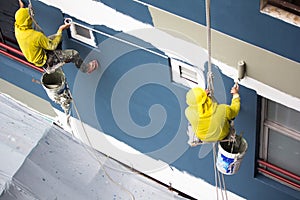 Painters hanging on roll, painting color on building wall