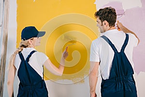 Painters in uniform looking at each other while painting wall in yellow and pink