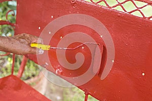 Painting the back rest of an old glider swing made of wrought iron with red oxide primer paint. Using a small paint roller.