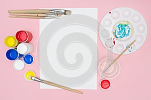 Painting brushes, colorful paints, and palette on pink background. Copy space. clipboard mockup. Artist workspace. Text.