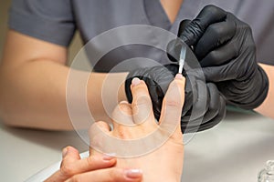 Painting female nails. Hands of manicurist in black gloves is applying transparent nail polish on female nails in a