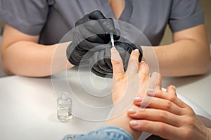 Painting female nails. Hands of manicurist in black gloves is applying transparent nail polish on female nails in a