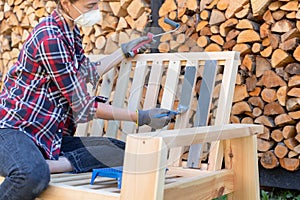 Painting garden furniture with paintbrush and roller with firewood in background. Protected from fumes with a respirator