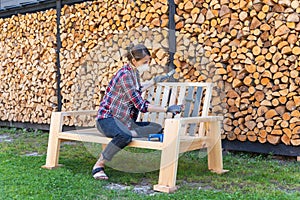 Painting garden furniture with paintbrush and roller with firewood in background. Protected from fumes with a respirator