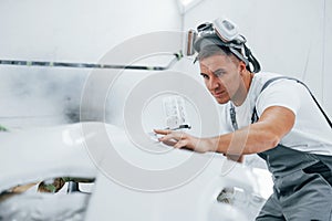 With painting gun. Caucasian automobile repairman in uniform works in garage