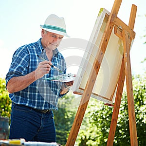 Painting is his favourite pasttime. a senior man painting in the park.