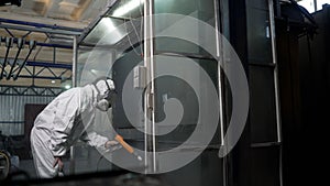 Painting metal with a spray gun, close-up. A worker in protective overalls works with hazardous chemicals, spraying them