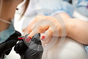 Painting nails of a woman. Hands of Manicurist in black gloves applying red nail polish on female Nails in a beauty