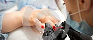 Painting nails of a woman. Hands of Manicurist in black gloves applying red nail polish on female Nails in a beauty