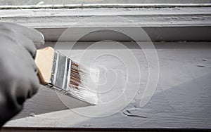 Painting old wooden window with white color. Brush in hand with grey glove