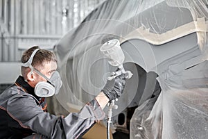 Painting the rear part of the car. Car painter wearing costume and protective gear. Car service station. Restoring a car