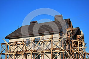 Painting, Stucco and Plastering Exterior House Scaffolding Facade Wall with New Metal Roofing Outdoor.