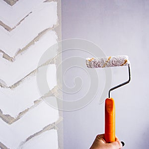 Painting a wall with masking tape. white zigzag strips on grey wall. hand holding the roller with paint