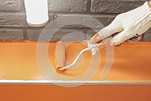 Painting wall orange with a white hand and paint roller close-up.