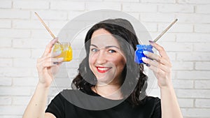 Painting in watercolors. Video portrait of laughing girl painter in a light studio with glass jar of paint in her hands