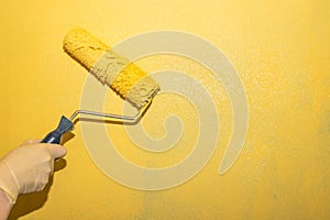Painting work. A woman paints the wall with a roller yellow paint, on the right is a copy of the space. The trend color of the
