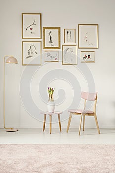 Paintings in golden frames, pink chair, table and lamp set on th