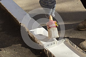 Paints the kerb with white paint. Brush with paint for the road curb