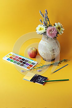 Paints, notebook and pencils, vase of flowers