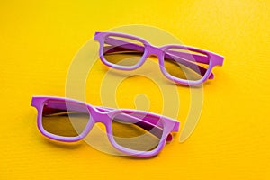 A pair of 3d glasses for watching a movie lie on a yellow background.