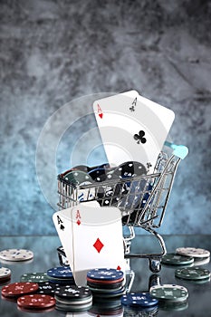A pair of aces, hearts and diamonds, on a deck of playing cards. Poker playing chips in a blue shopping cart