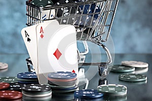 A pair of aces, hearts and diamonds, on a deck of playing cards. Poker playing chips in a blue shopping cart