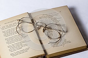 A pair of Antique Eyeglasses sitting on a opened vintage hymnal on a white background