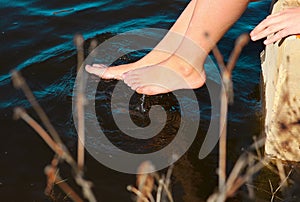 Pair of bare feet touch dark blue water