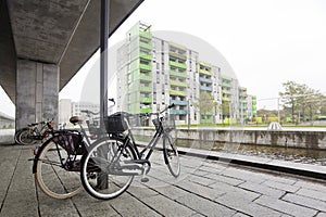 A pair of bicycles on the bank of a canal under a concrete pillar in Copenhagen
