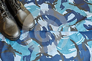 A pair of black army boots on fabric with blue camouflage with copispace for text