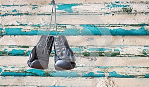 Pair of black boxing gloves hanging on an old rustic wooden wall.