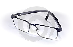 Pair of black thin rimmed spectacles resting half closed at slight angle on white background