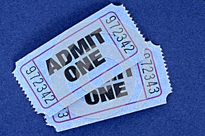 Pair of blue admit one movie tickets on a blue background.