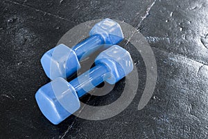 A pair of blue hard plastic hex dumbbells lying on the rubber matted floor of a gym or health club.