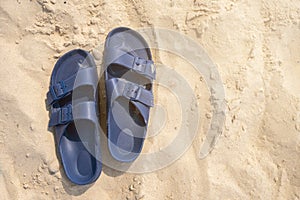 Pair of blue plastic buckled sandals or flip-flops on a beach sand with copy space