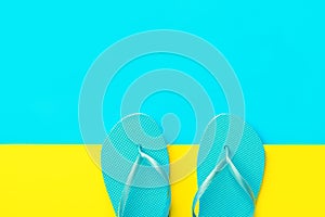 Pair of blue rubber beach slippers on duotone bright yellow cyan background. Imitation of sand and sea. Creative flat lay. Summer