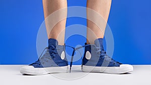 A pair of blue sneakers connected with laces on women`s legs. Shoes for sports and travel.