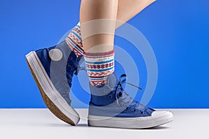 A pair of blue sneakers connected with laces on women`s legs. Shoes for sports and travel.