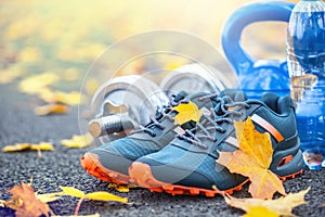 Pair of blue sport shoes water and dumbbells laid on a path in a tree autumn alley with maple leaves - accessories for run exerc photo