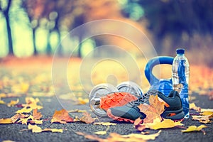 Pair of blue sport shoes water and dumbbells laid on a path in a tree autumn alley with maple leaves - accessories for run exerc